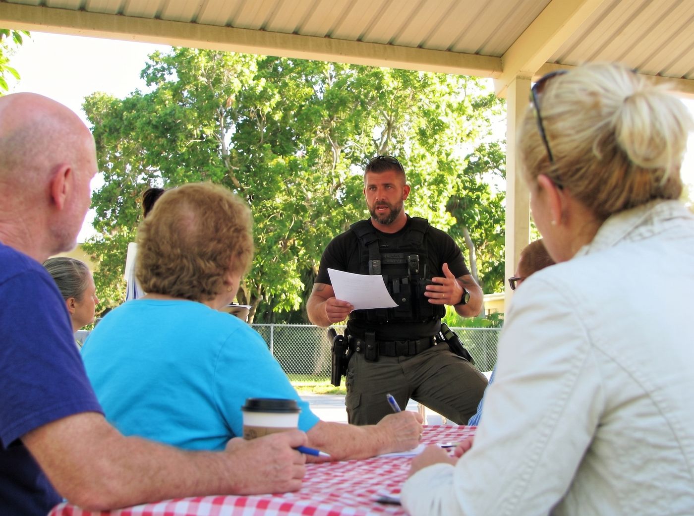 A law enforcement officer briefing residents at an outdoor Neighborhood Watch meeting